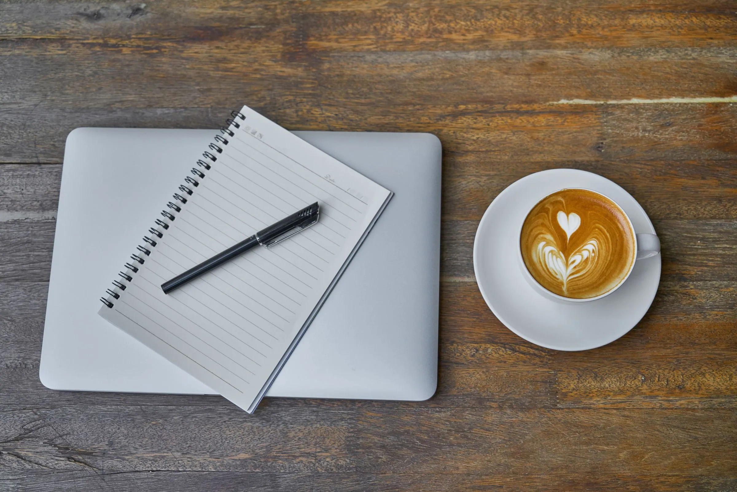 Schreibtisch mit Notizbuch, Stift und einer Tasse Kaffee