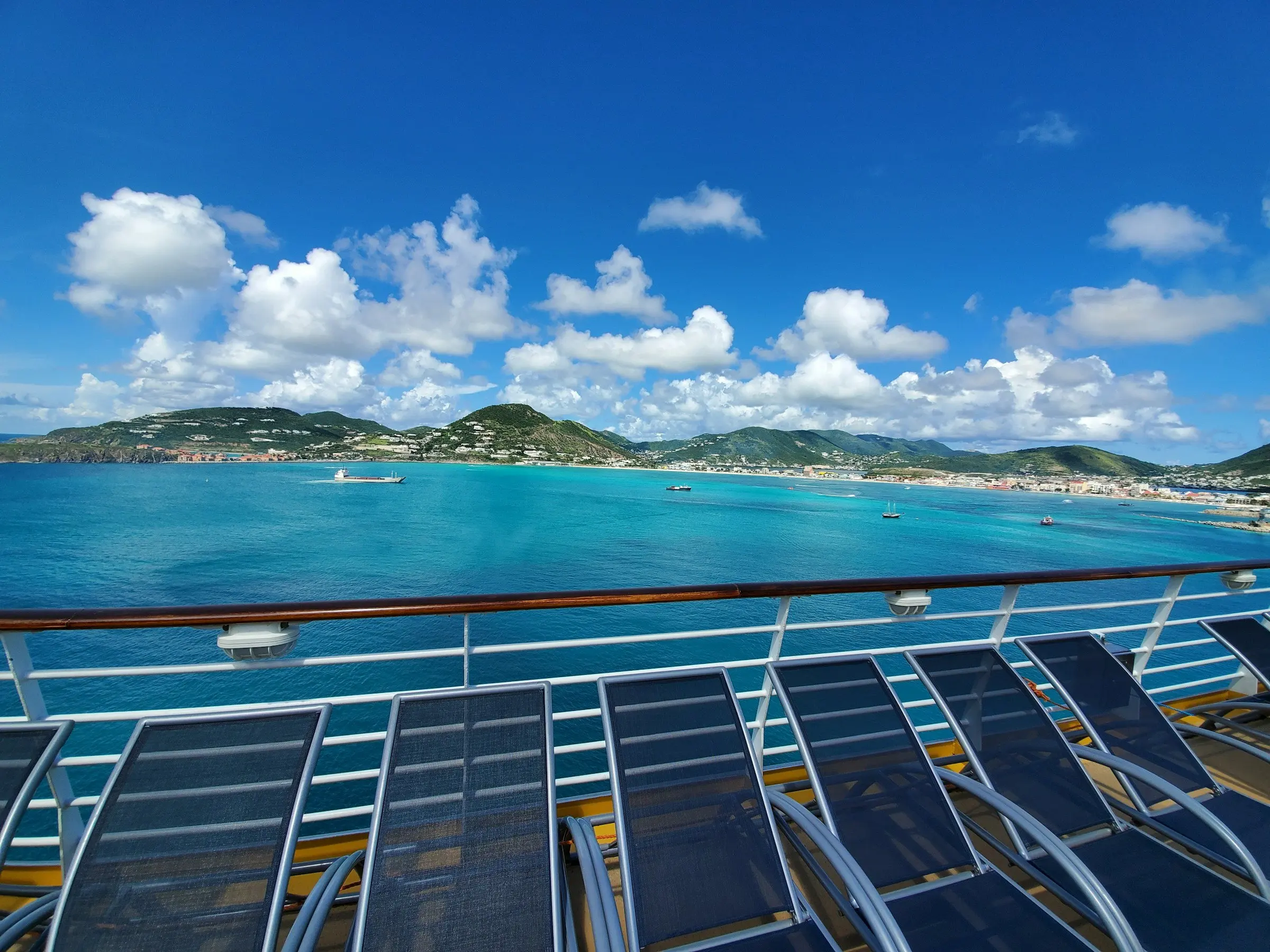 Sonnendeck eines Schiffes mit leeren Liegestühlen, dahinter eine Bucht