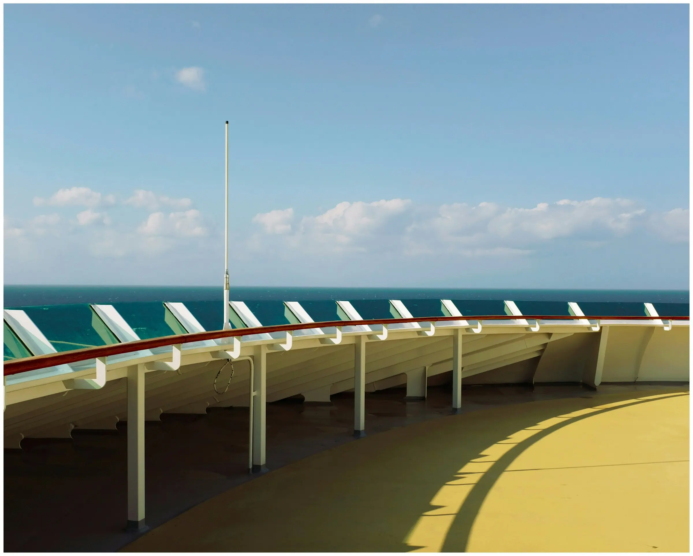 Geschwungene Reling eines Schiffsdecks, dahinter das offene Meer