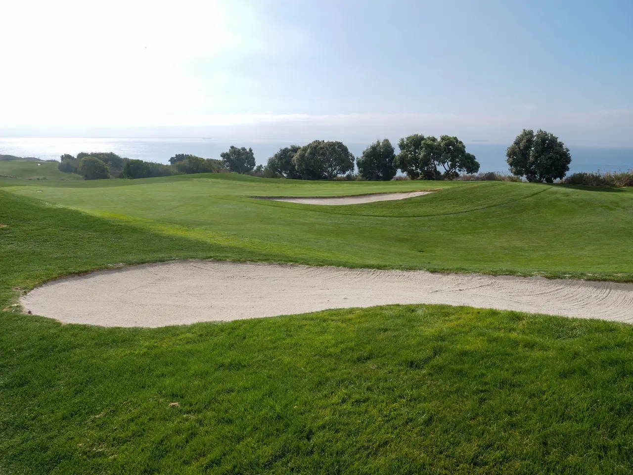 Golfplatz mit Sandbunker und Blick auf das Meer
