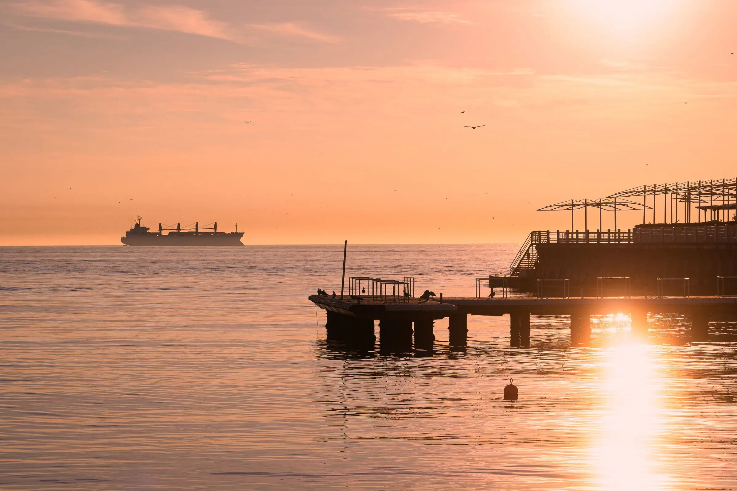 Steg am Wasser bei Sonnenaufgang, in der Ferne ein Schiff