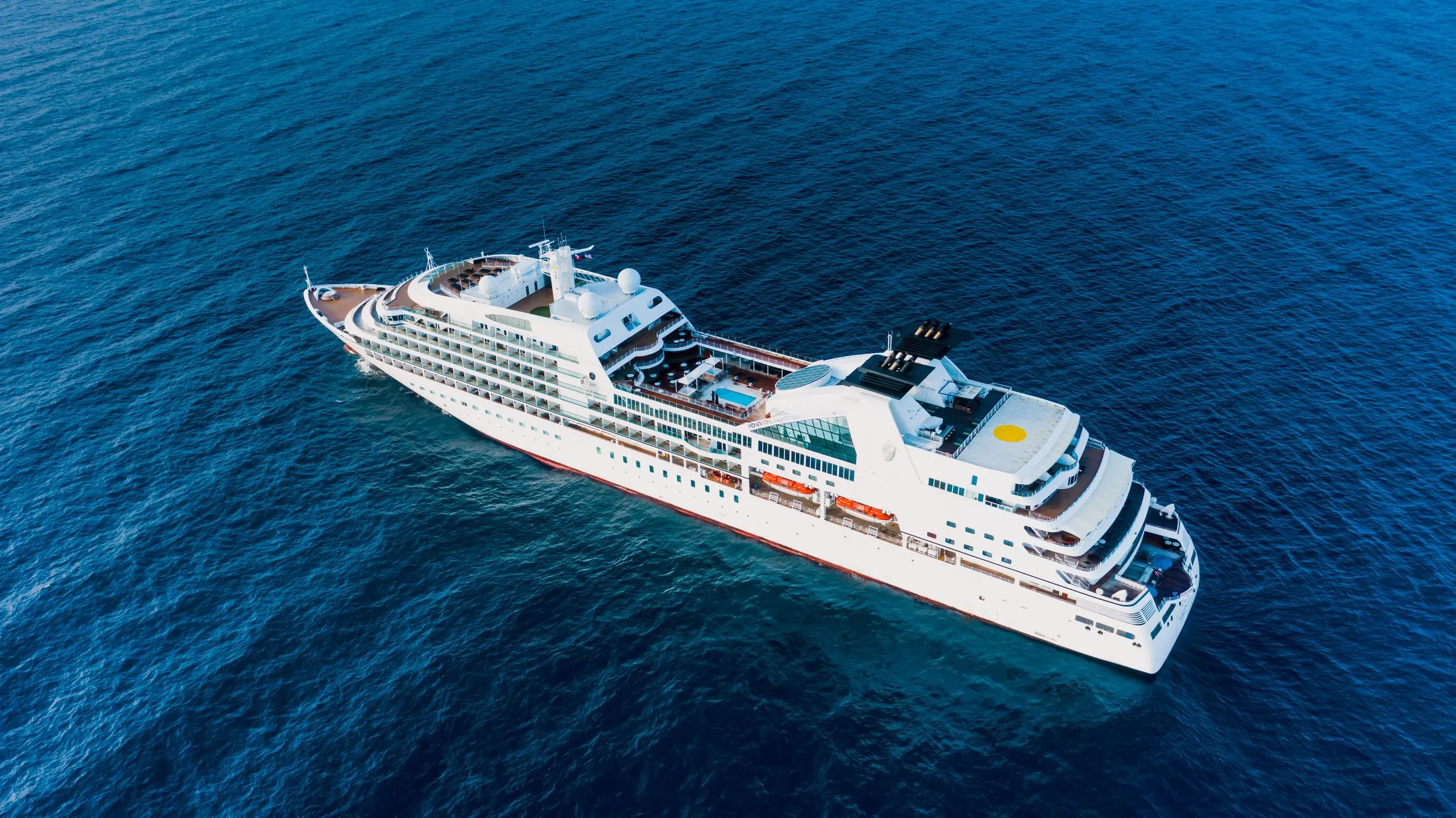 Weißes Hochsee-Kreuzfahrtschiff schräg von oben auf tiefblauem, offenem Meer